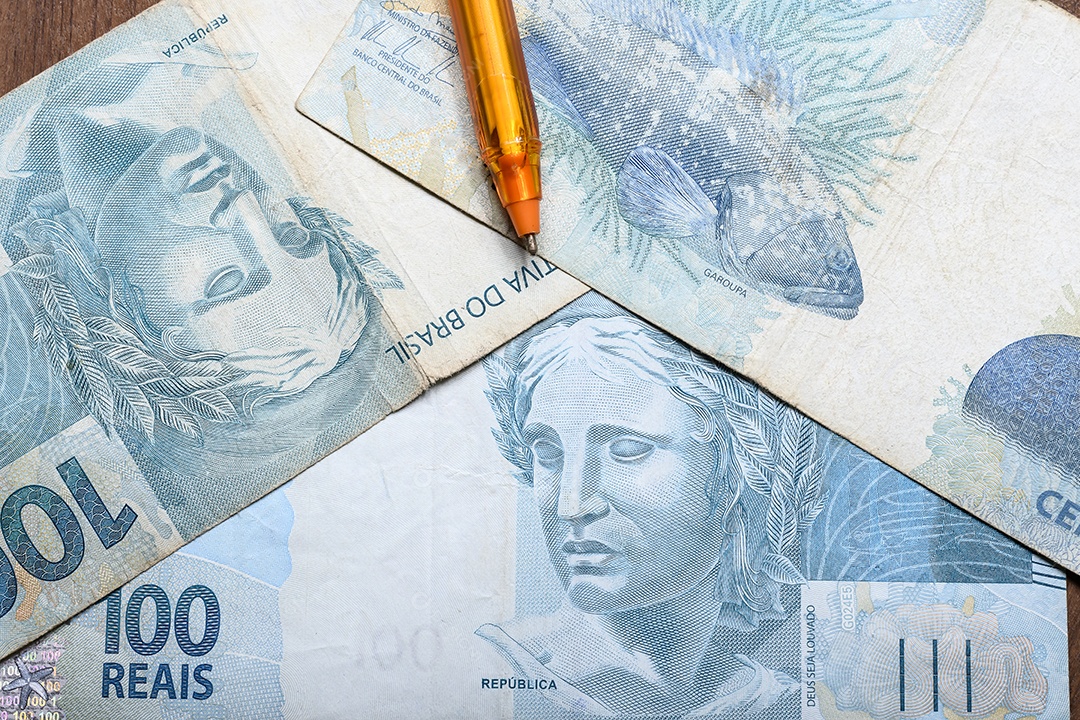 Cédulas de cem reais com caneta em cima