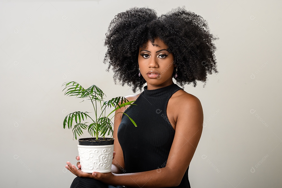 Mulher negra segurando um vaso com uma planta pequena