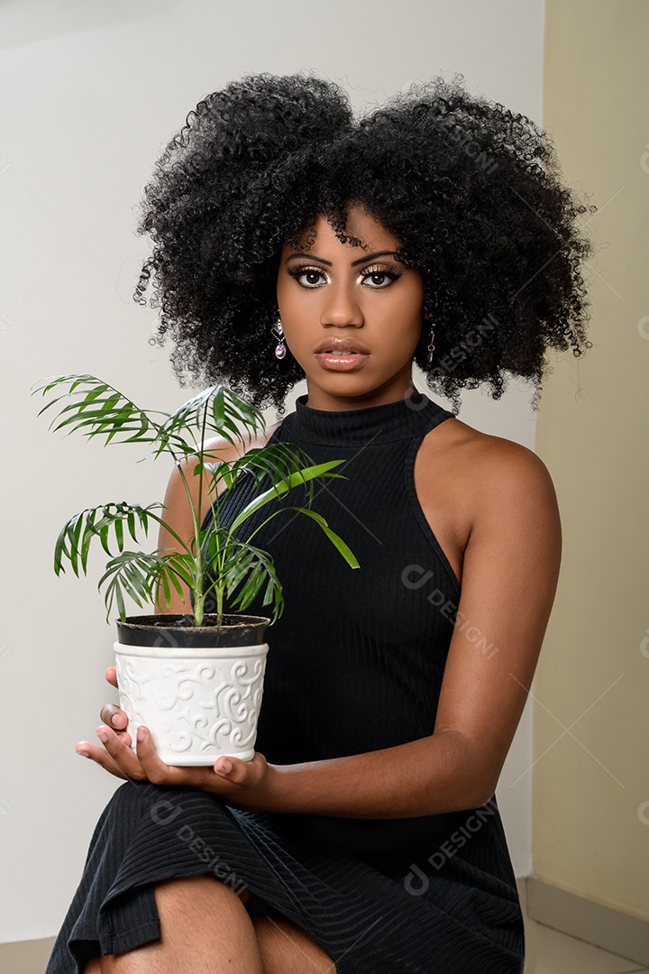 Mulher negra segurando um vaso com uma planta pequena