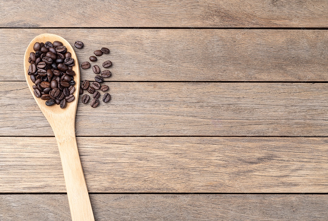 Colher de madeira cheia de café em grãos sobre mesa rustica