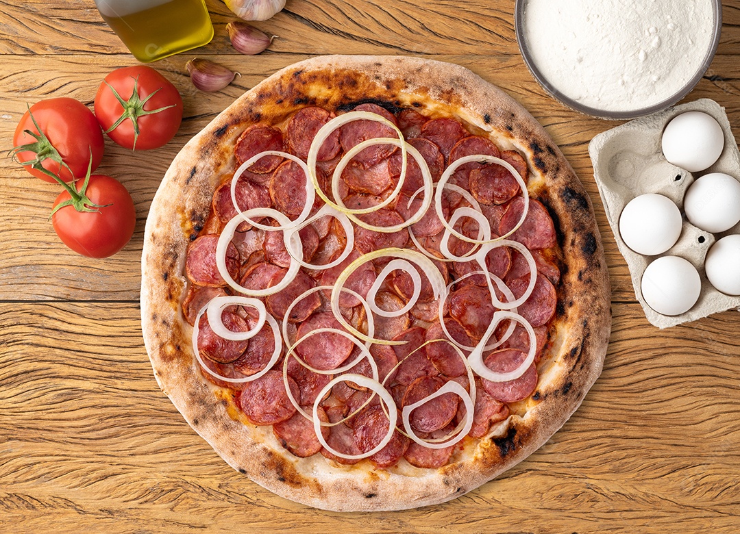 Pizza de calabresa acebolada tomates ovos farinha e azeite sobre fundo de madeira