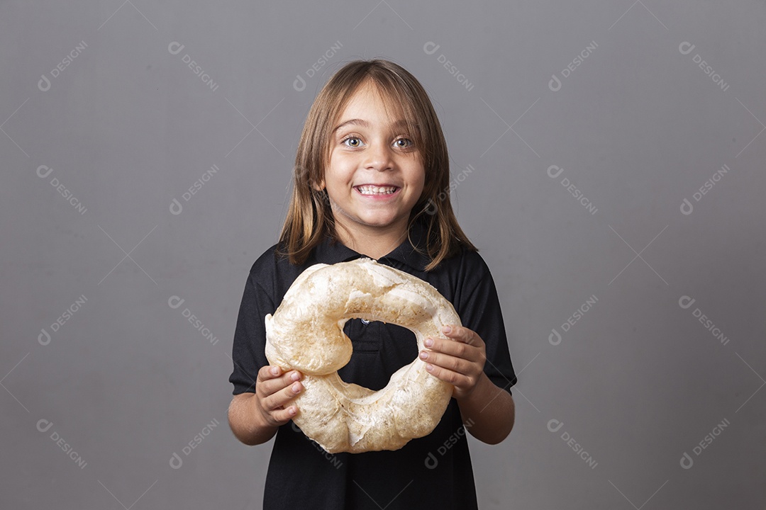 Criança sorridente segurando biscoito rosca de polvilho sobre fundo isolado