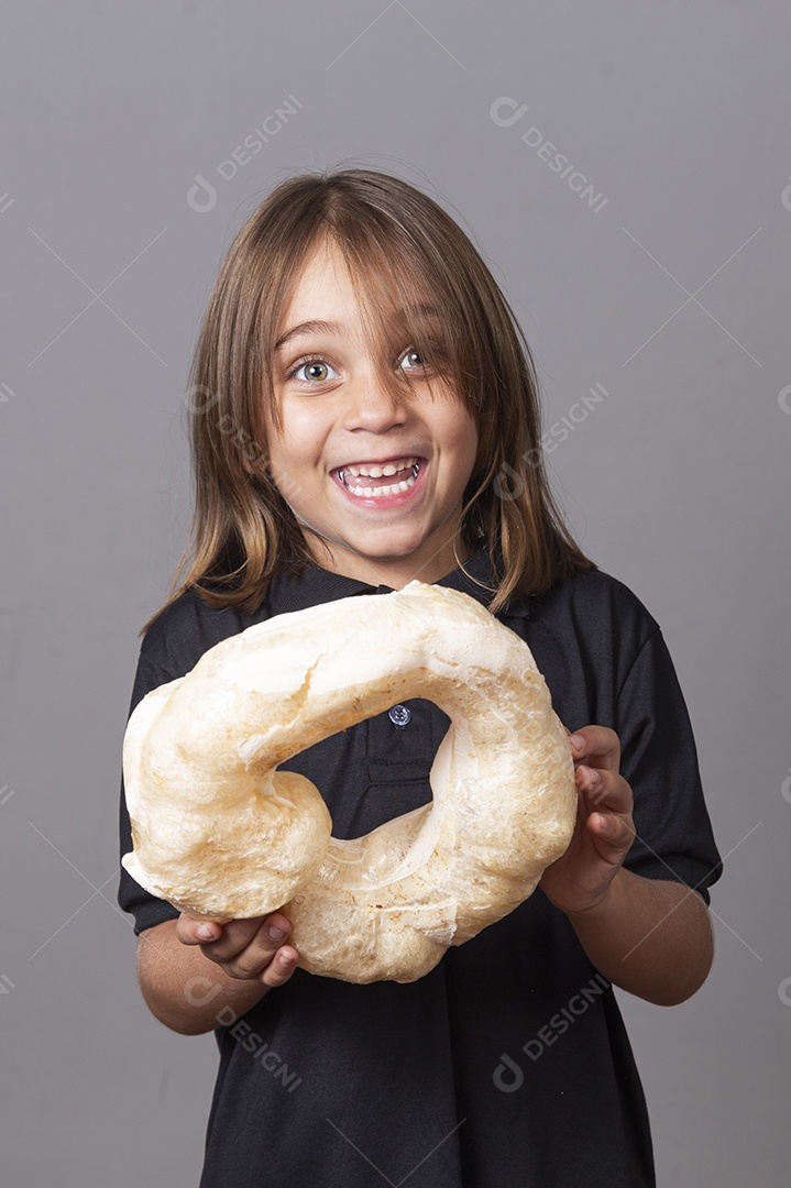 Criança sorridente segurando biscoito rosca de polvilho sobre fundo isolado