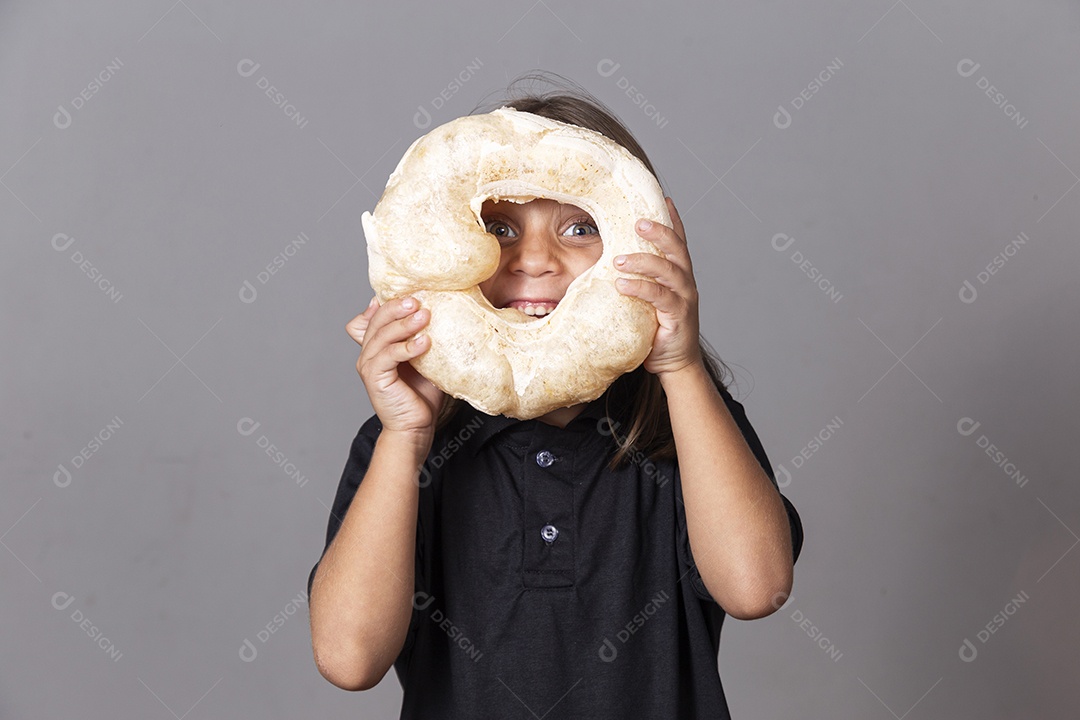 Criança segurando biscoito rosca de polvilho sobre o rosto