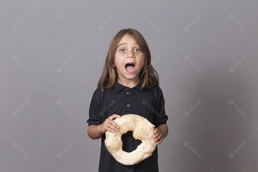 Criançade boca aberta segurando biscoito rosca de polvilho sobre fundo isolado