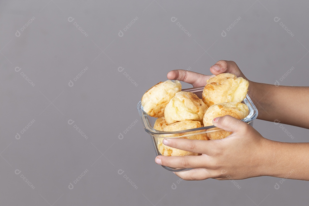 Mãos segurando travessa de pães de queijo sobre fundo isolado