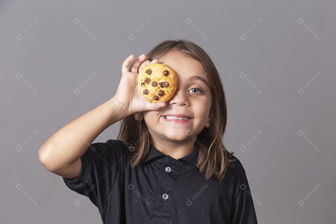 Garoto sorridente segurando bolacha sobre o olho