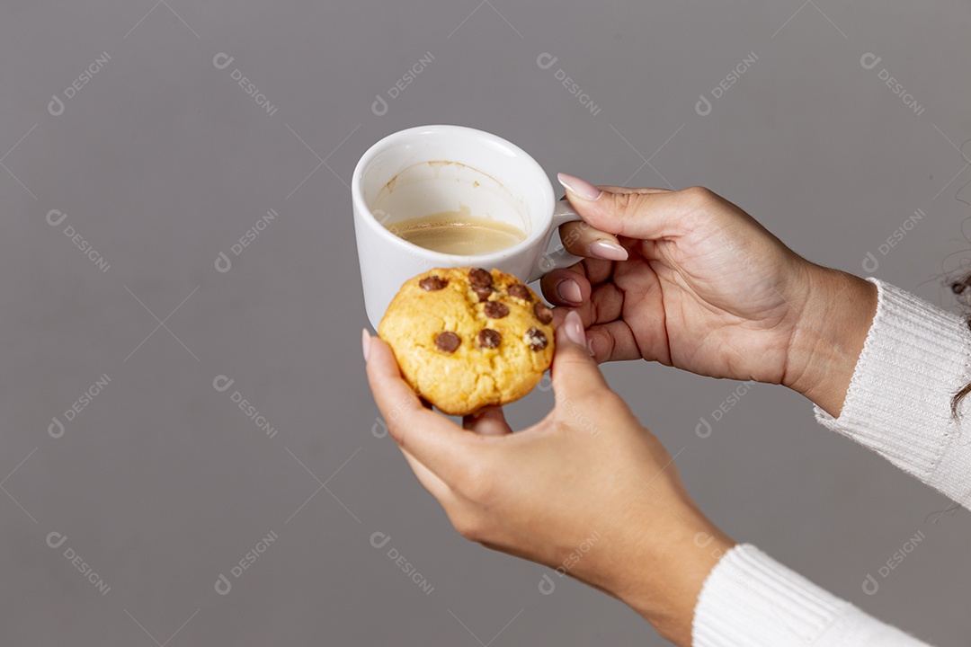 Mãos segurando xicara e um cookie sobre fundo isoaldo
