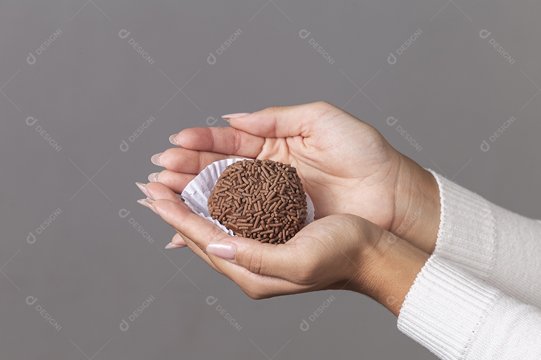 Mãos segurando brigadeiro sobre fundo isolado.