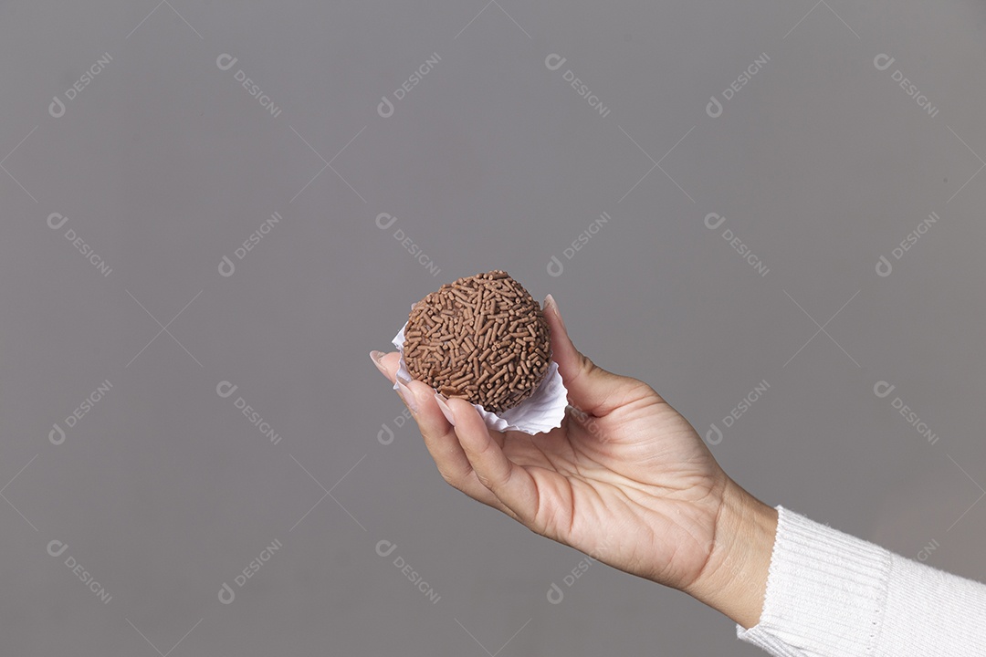 Mão segurando brigadeiro sobre fundo isolado.