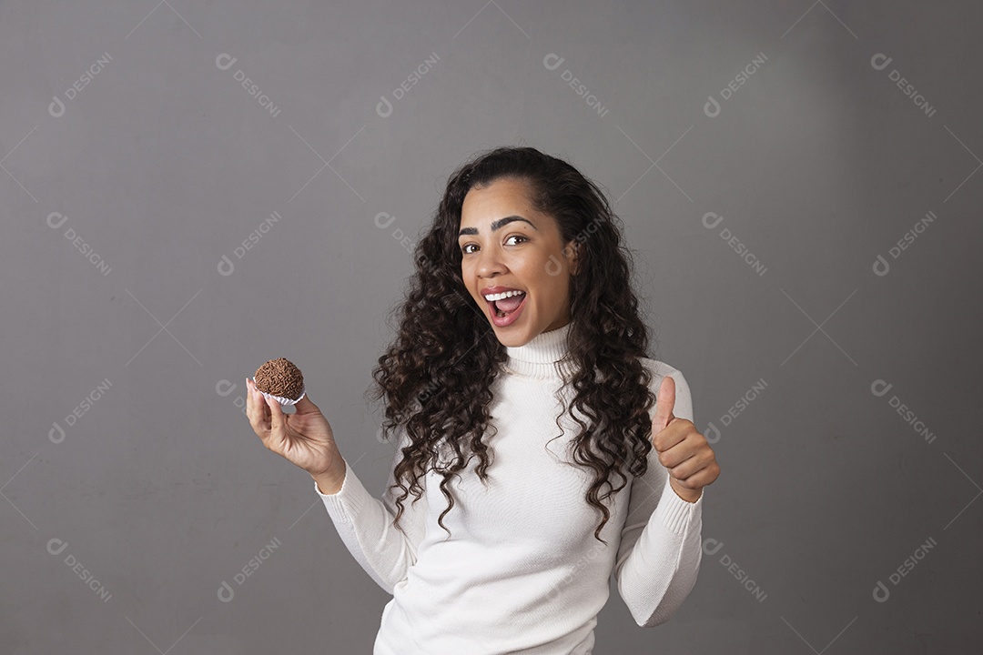 Linda mulher de cabelo cacheado segurando um cupcake sobre um fundo isolado.