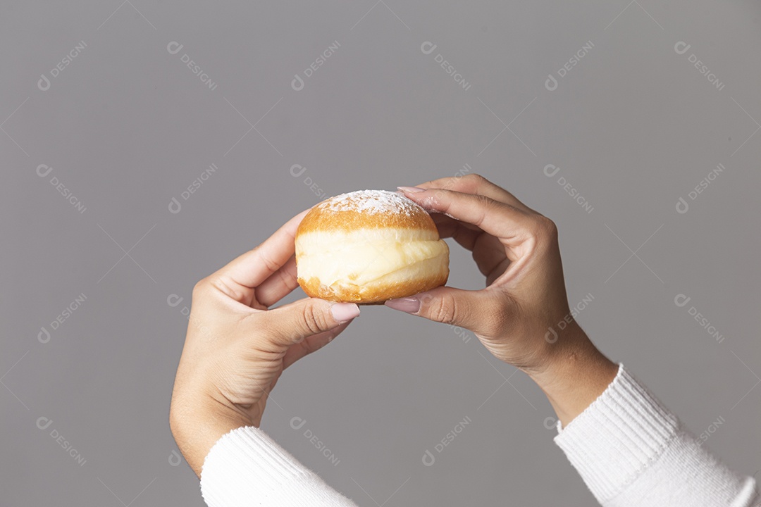 Mãos segurando um delicioso sonho de padaria sobre fundo isolado