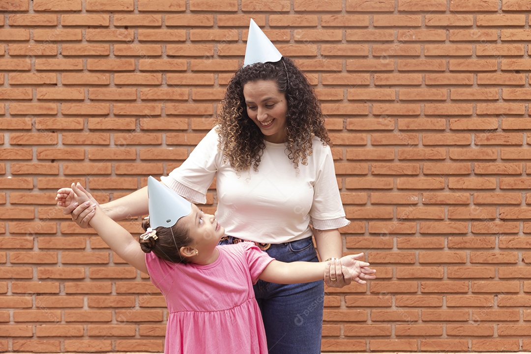 Mãe ao lado de sua filha felizes usando chapéu de aniversário