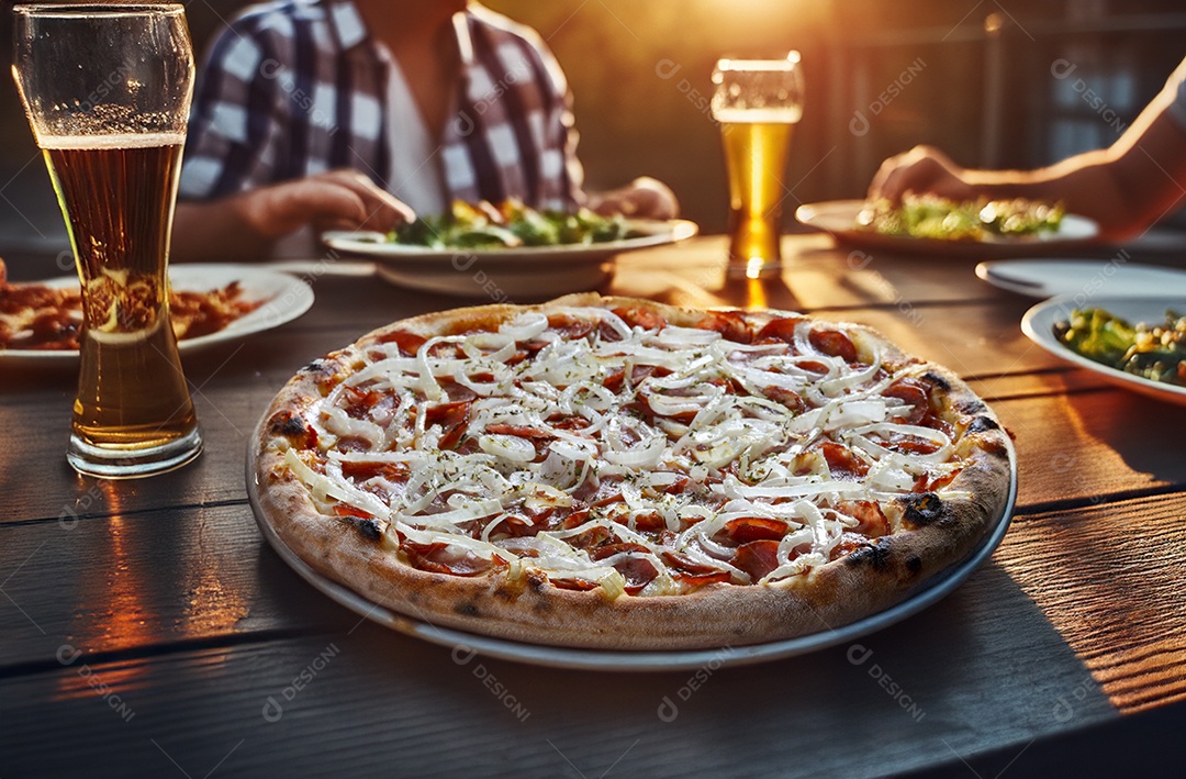 Pizza sobre uma mesa com copos de cervejas e amigos reunidos