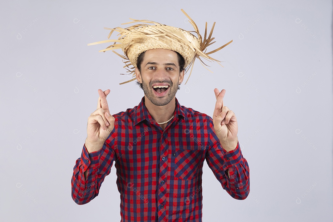 Homem jovem usando roupas típicas de festa junina dedos cruzados sobre fundo isolado