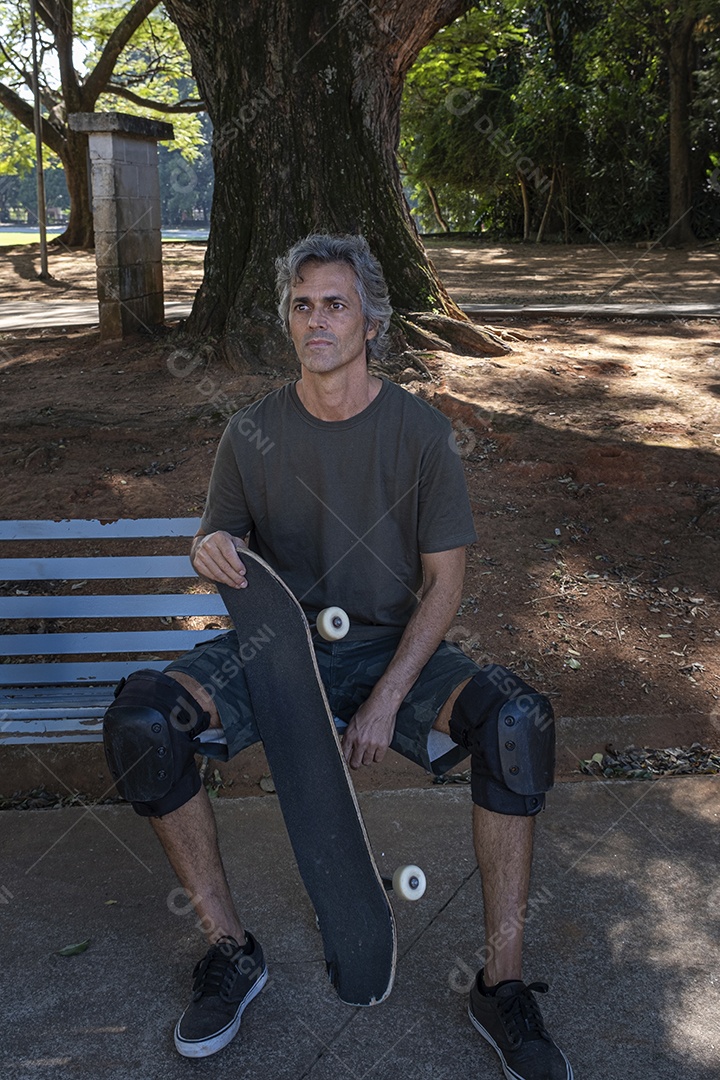 Homem skatista descansando em praça cheia de árvores