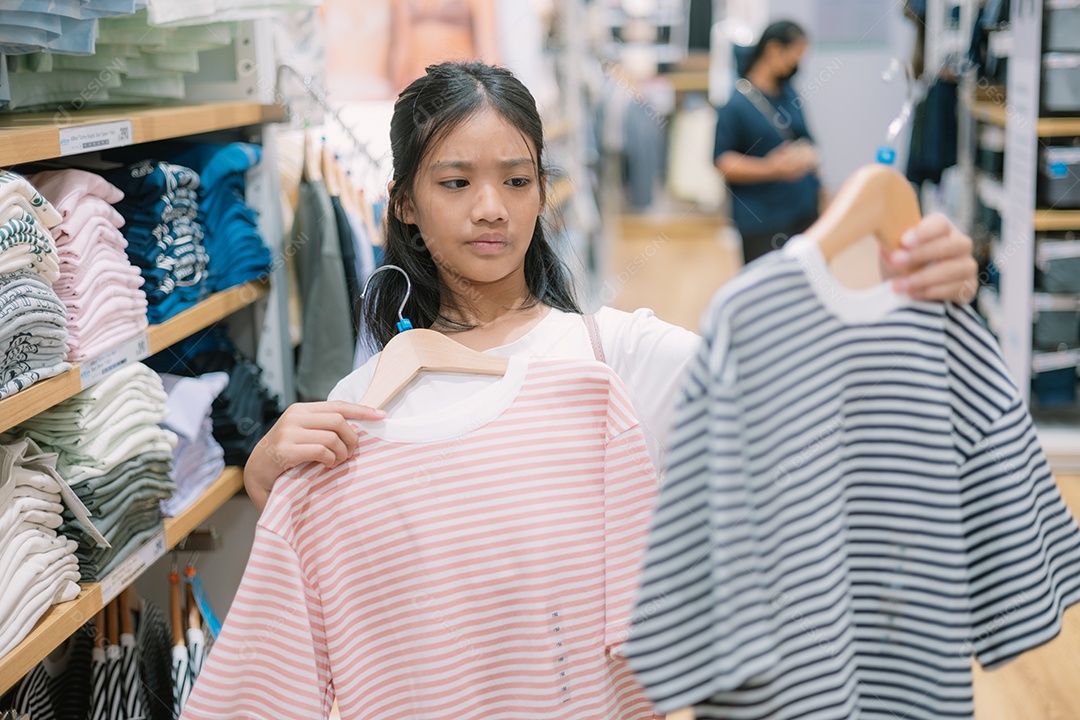 Menina julgando peças de roupa em loja