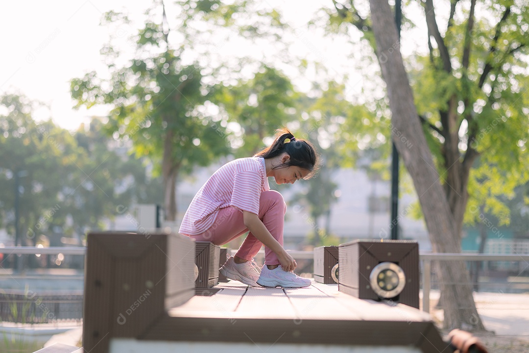 Menina amarrando tênis sentada em um banco de praça