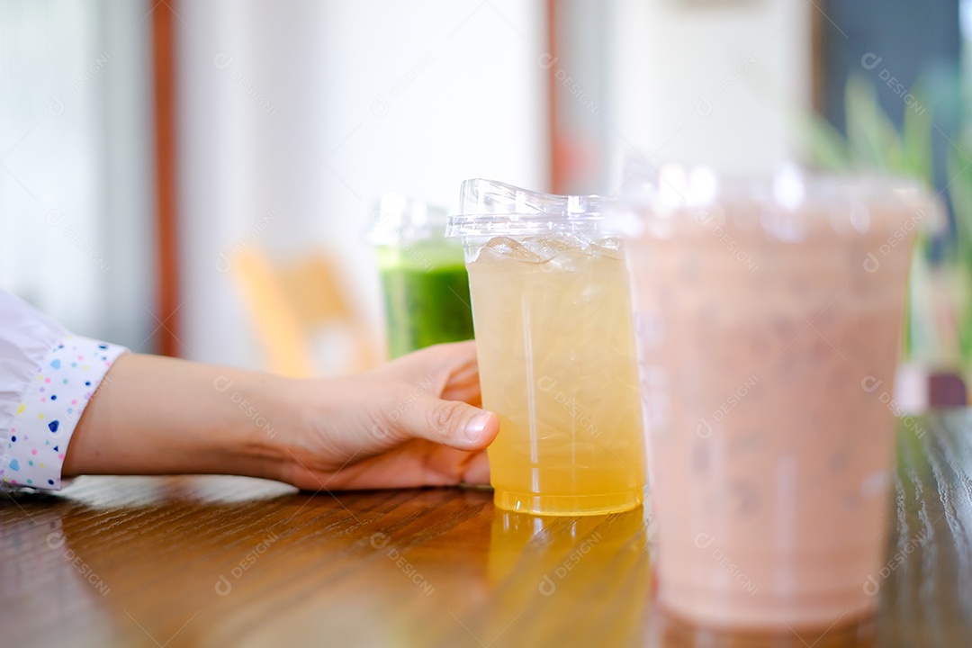 A mão da mulher segura um copo de plástico muito doce ou café sobre o fundo da mesa