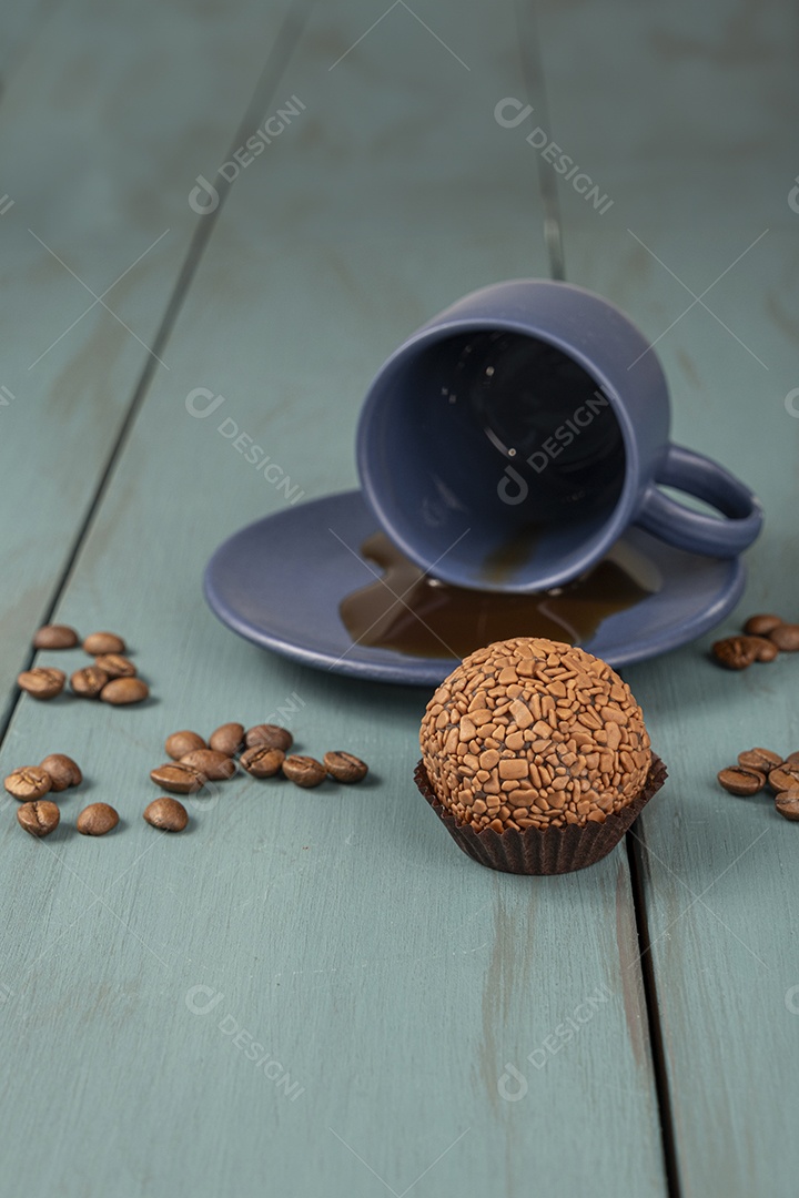 Xícara de café e brigadeiro de chocolate com grãos ao fundo
