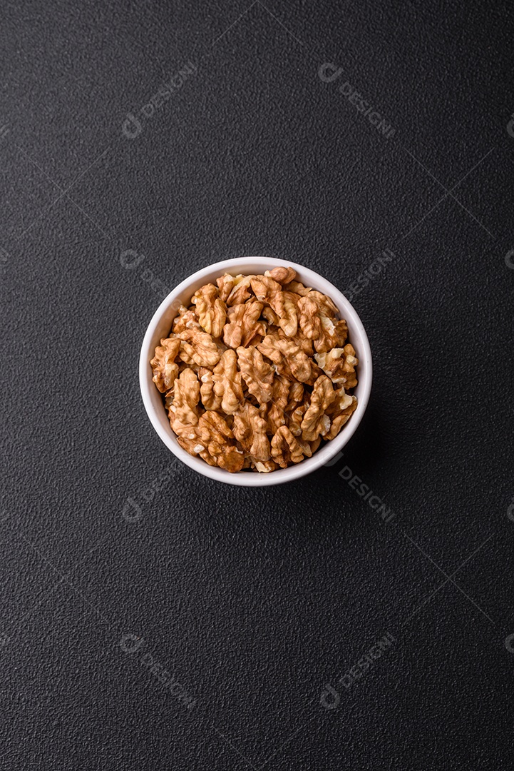 Deliciosas nozes cruas descascadas frescas em uma placa cerâmica sobre um fundo escuro de concreto