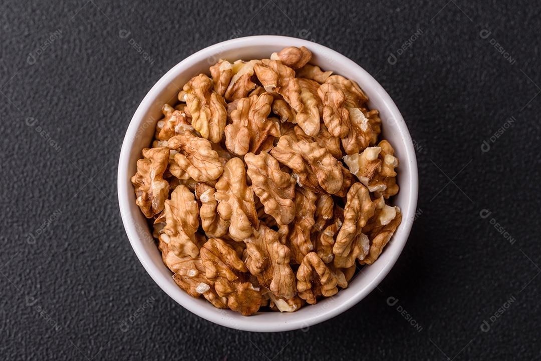 Deliciosas nozes cruas descascadas frescas em uma placa cerâmica sobre um fundo escuro de concreto