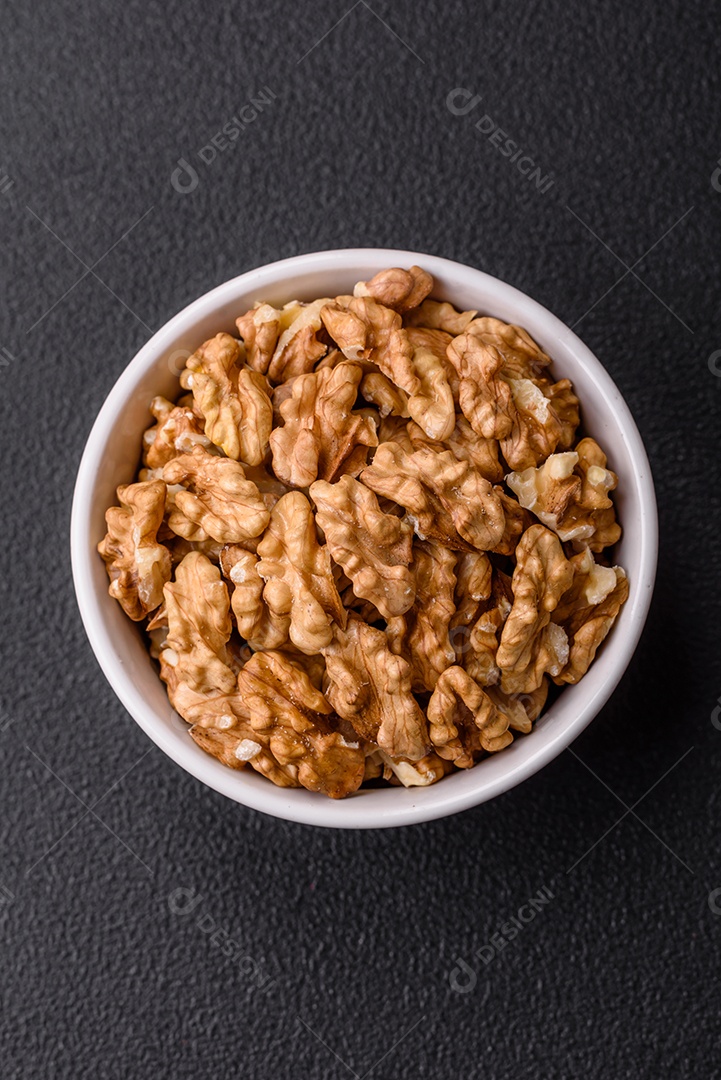 Deliciosas nozes cruas descascadas frescas em uma placa cerâmica sobre um fundo escuro de concreto