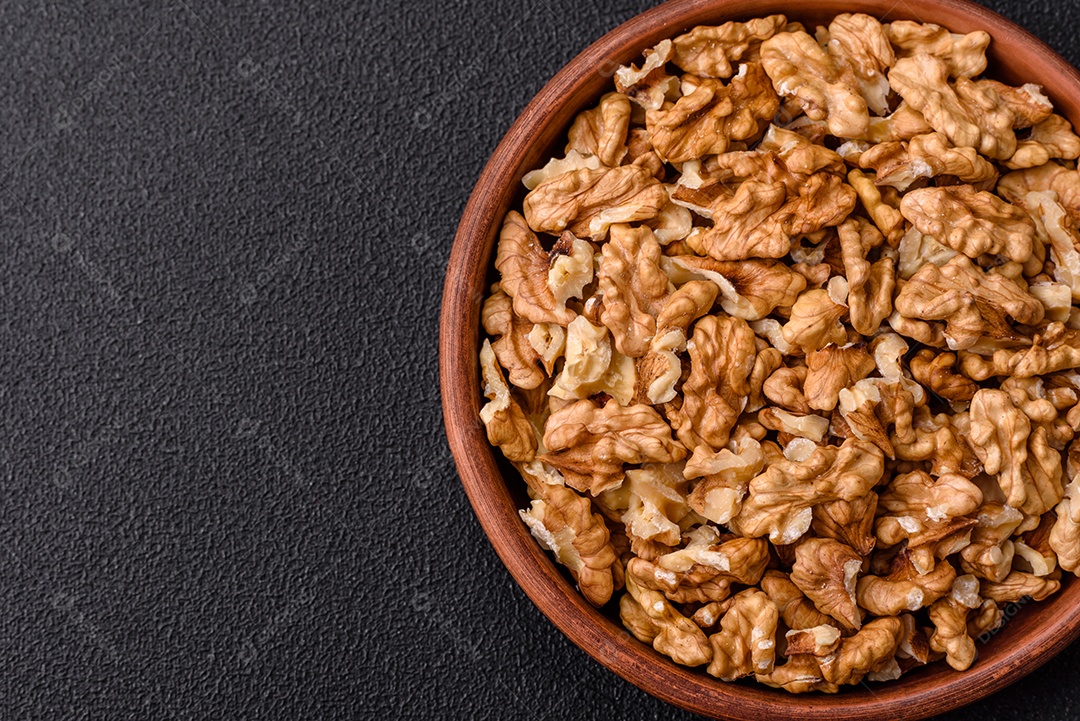 Deliciosas nozes cruas descascadas frescas em uma placa cerâmica sobre um fundo escuro de concreto