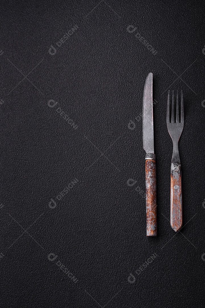 Garfo de talheres, faca e colher sobre um fundo de concreto texturizado escuro. Itens e acessórios de cozinh