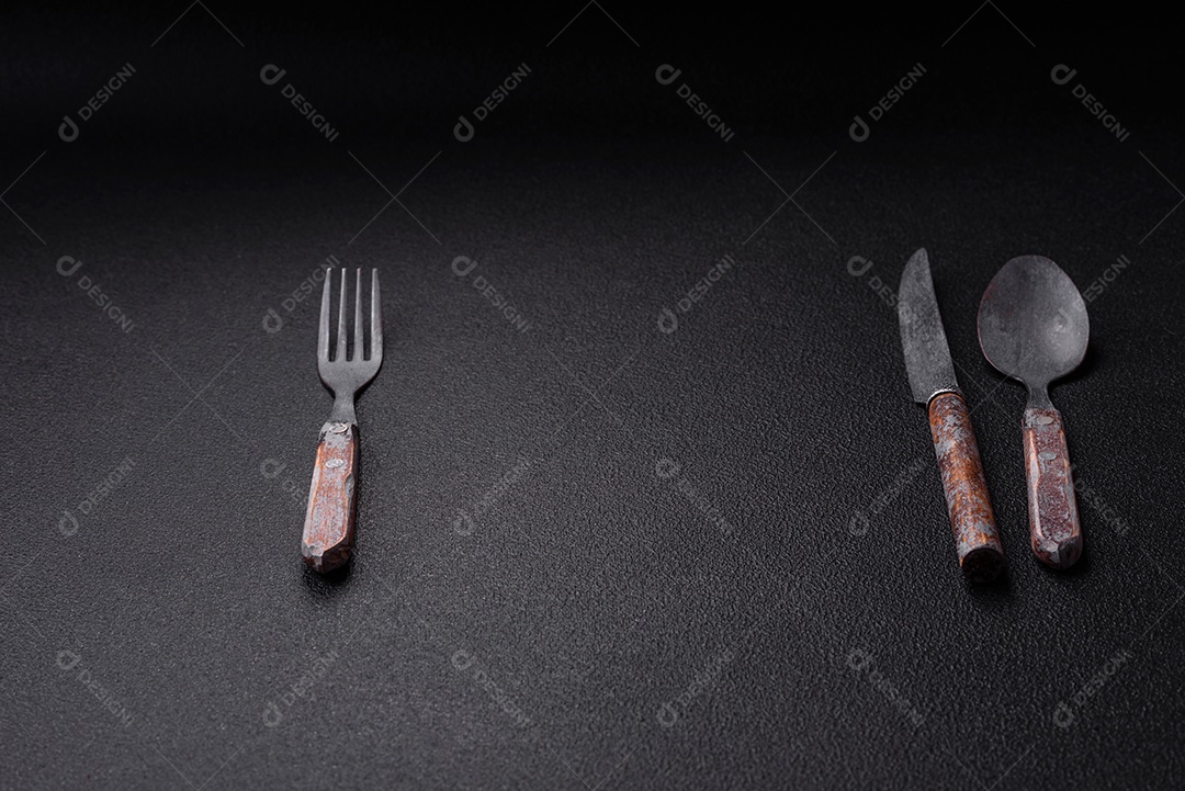 Garfo de talheres, faca e colher sobre um fundo de concreto texturizado escuro. Itens e acessórios de cozinha