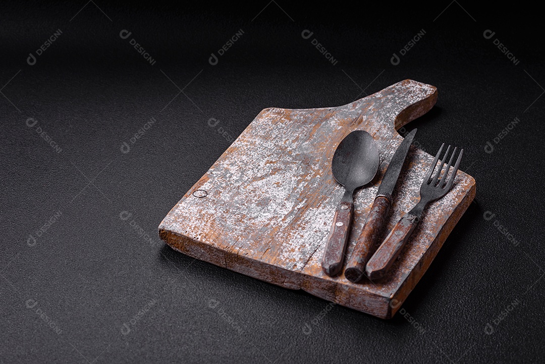 Garfo de talheres, faca e colher sobre um fundo de concreto texturizado escuro. Itens e acessórios de cozinha