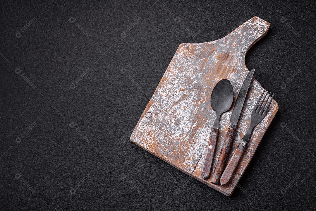 Garfo de talheres, faca e colher sobre um fundo de concreto texturizado escuro. Itens e acessórios de cozinha