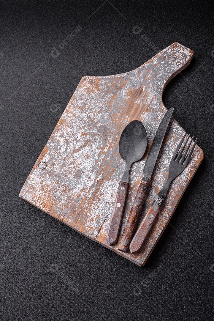 Garfo de talheres, faca e colher sobre um fundo de concreto texturizado escuro. Itens e acessórios de cozinha