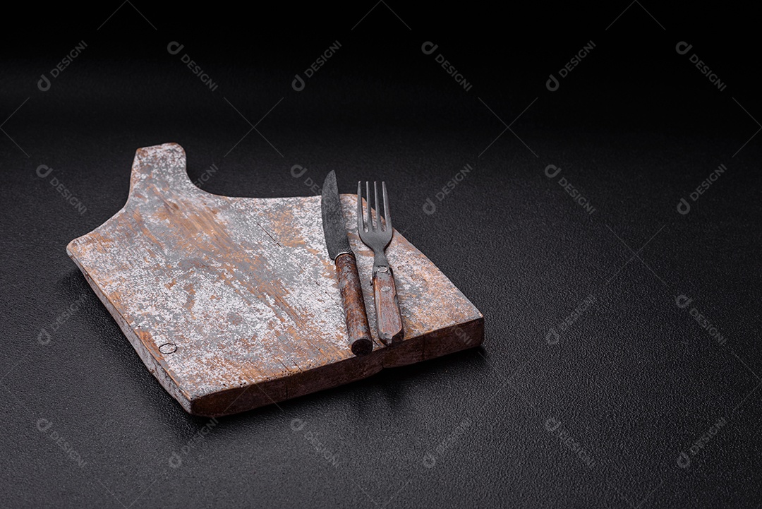 Garfo de talheres, faca e colher sobre um fundo de concreto texturizado escuro. Itens e acessórios de cozinha