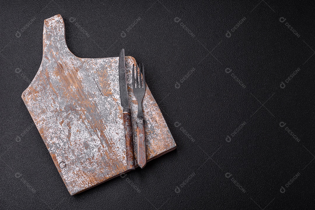 Garfo de talheres, faca e colher sobre um fundo de concreto texturizado escuro. Itens e acessórios de cozinha