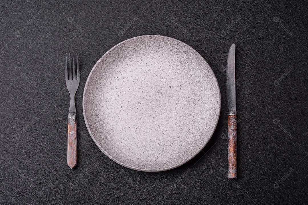 Garfo de talheres, faca e colher sobre um fundo de concreto texturizado escuro. Itens e acessórios de cozinha