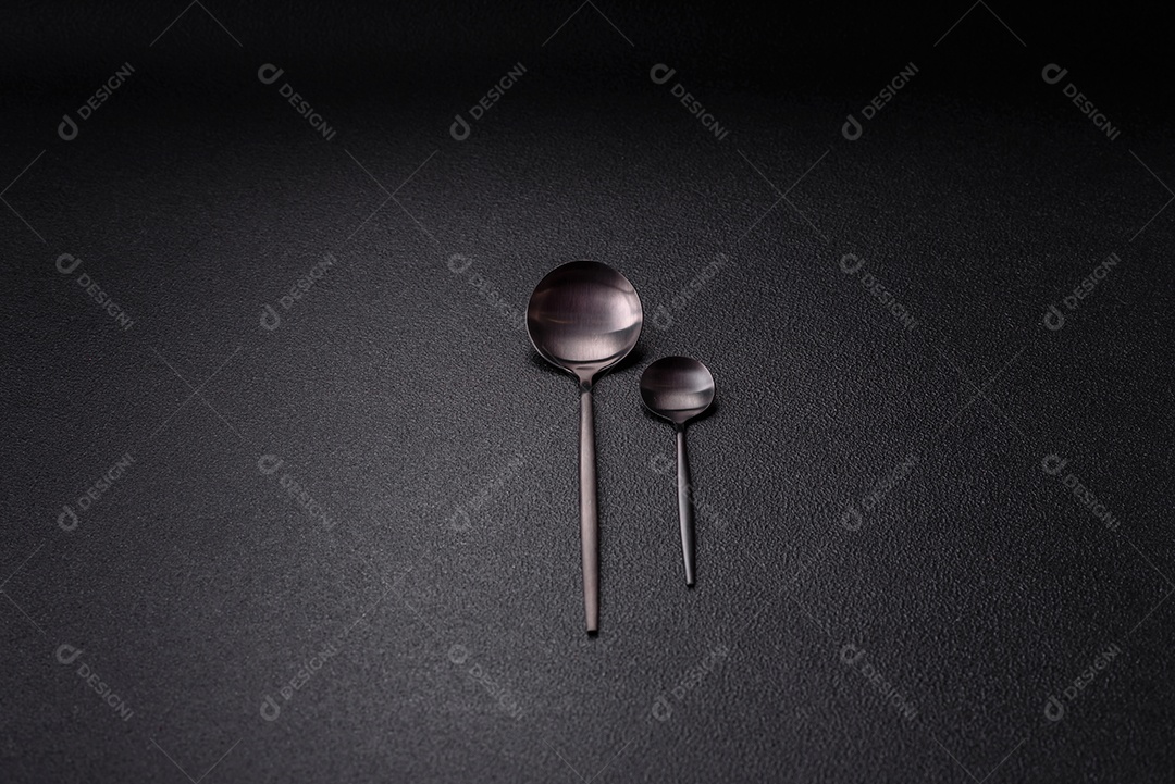 Garfo de talheres, faca e colher sobre um fundo de concreto texturizado escuro. Itens e acessórios de cozinha