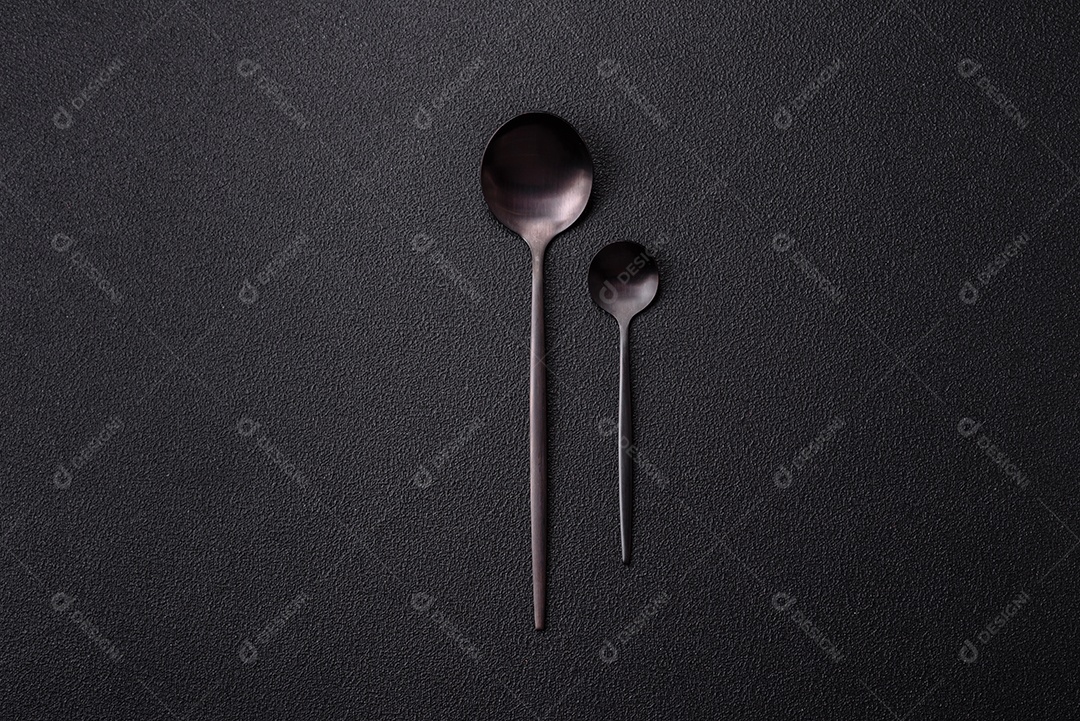 Garfo de talheres, faca e colher sobre um fundo de concreto texturizado escuro. Itens e acessórios de cozinha