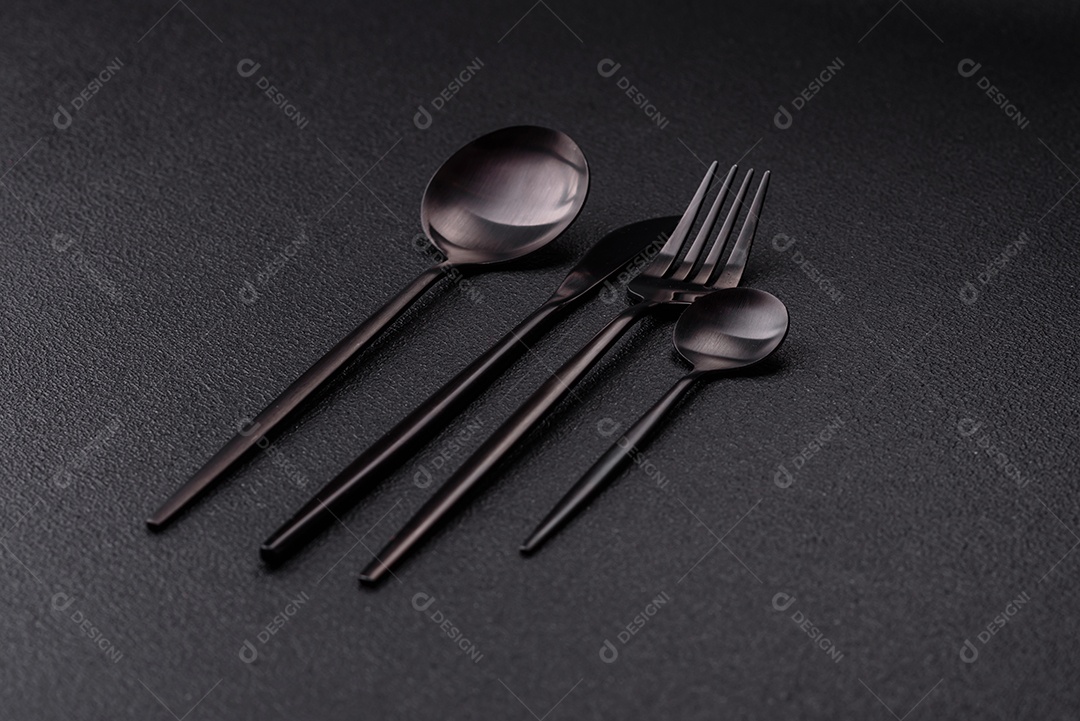 Garfo de talheres, faca e colher sobre um fundo de concreto texturizado escuro. Itens e acessórios de cozinha