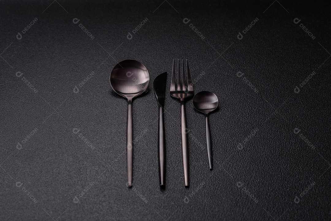 Garfo de talheres, faca e colher sobre um fundo de concreto texturizado escuro. Itens e acessórios de cozinha