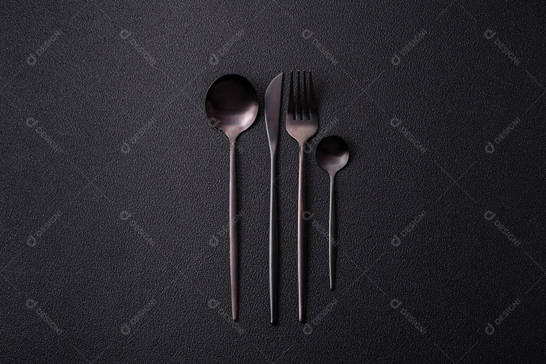 Garfo de talheres, faca e colher sobre um fundo de concreto texturizado escuro. Itens e acessórios de cozinha