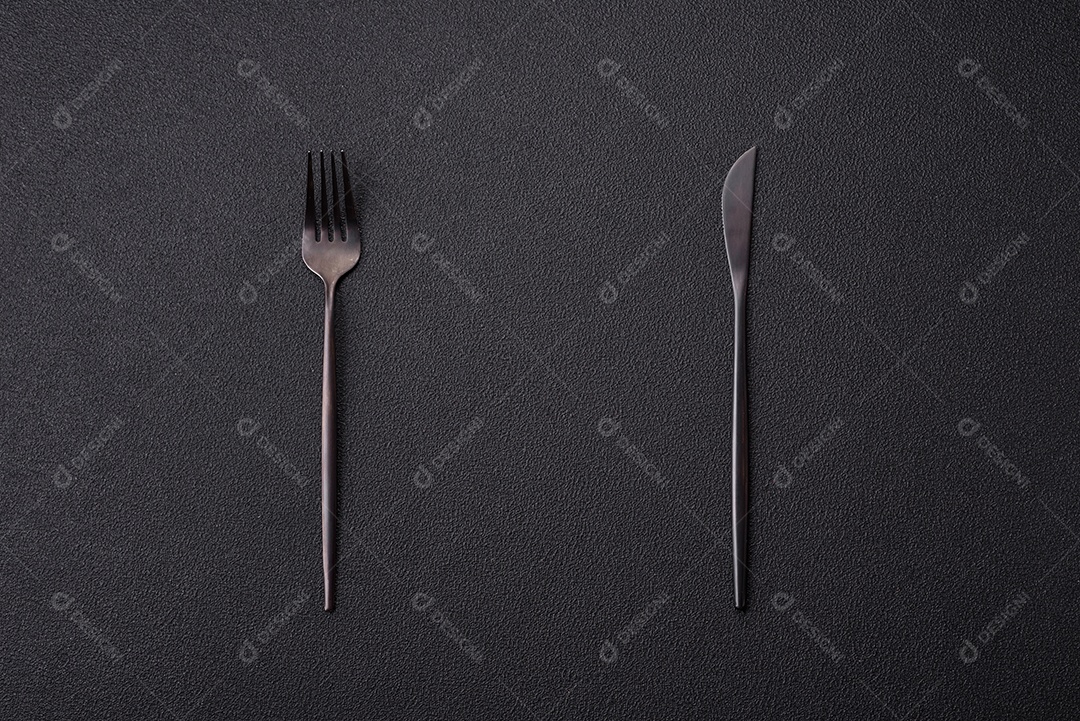 Garfo de talheres, faca e colher sobre um fundo de concreto texturizado escuro. Itens e acessórios de cozinha