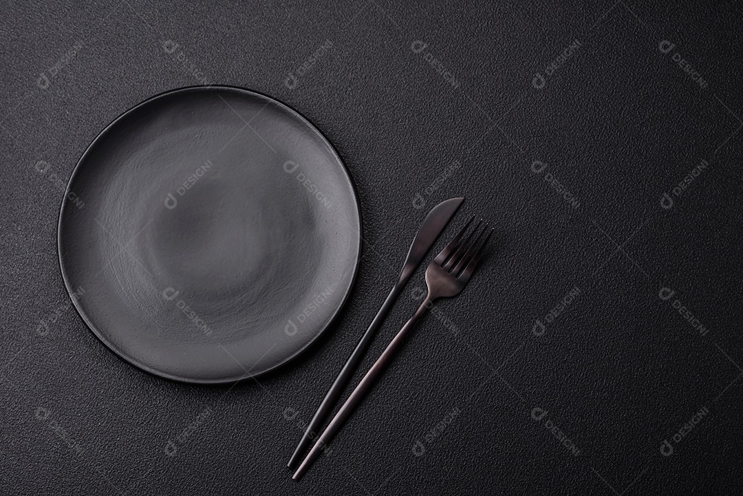 Garfo de talheres, faca e colher sobre um fundo de concreto texturizado escuro. Itens e acessórios de cozinha