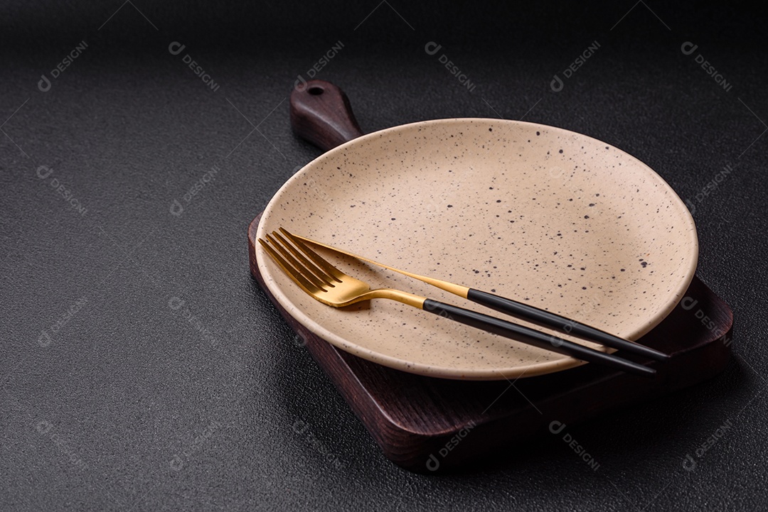 Garfo de talheres, faca e colher sobre um fundo de concreto texturizado escuro. Itens e acessórios de cozinha