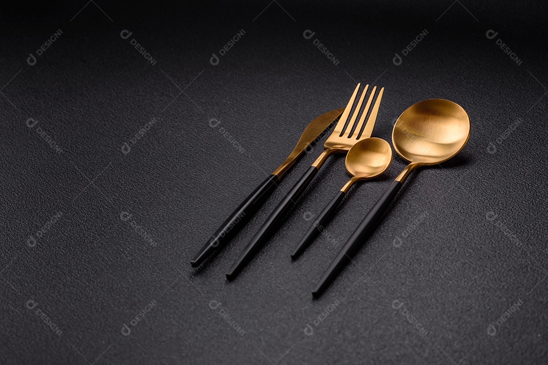 Garfo de talheres, faca e colher sobre um fundo de concreto texturizado escuro. Itens e acessórios de cozinha