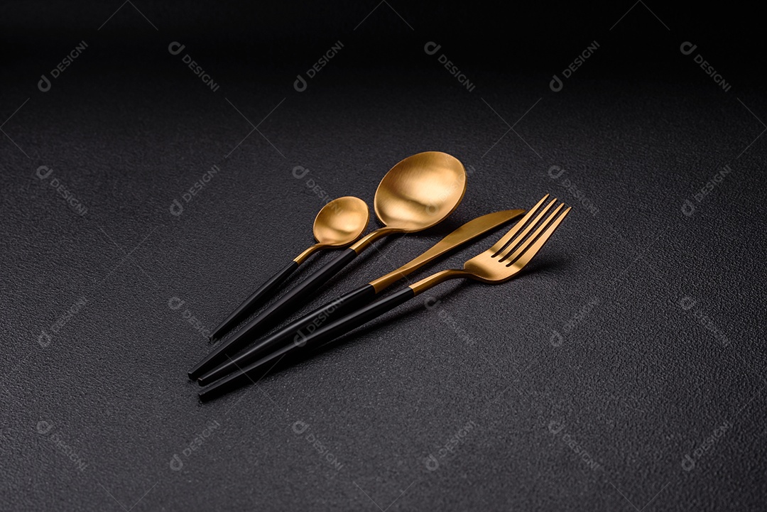 Garfo de talheres, faca e colher sobre um fundo de concreto texturizado escuro. Itens e acessórios de cozinha