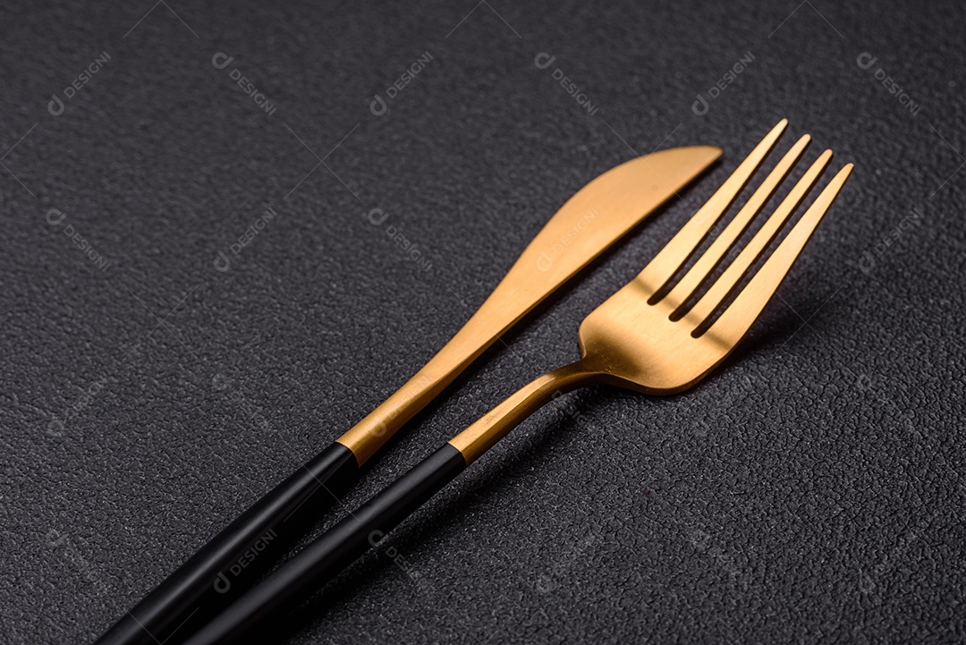 Garfo de talheres, faca e colher sobre um fundo de concreto texturizado escuro. Itens e acessórios de cozinha