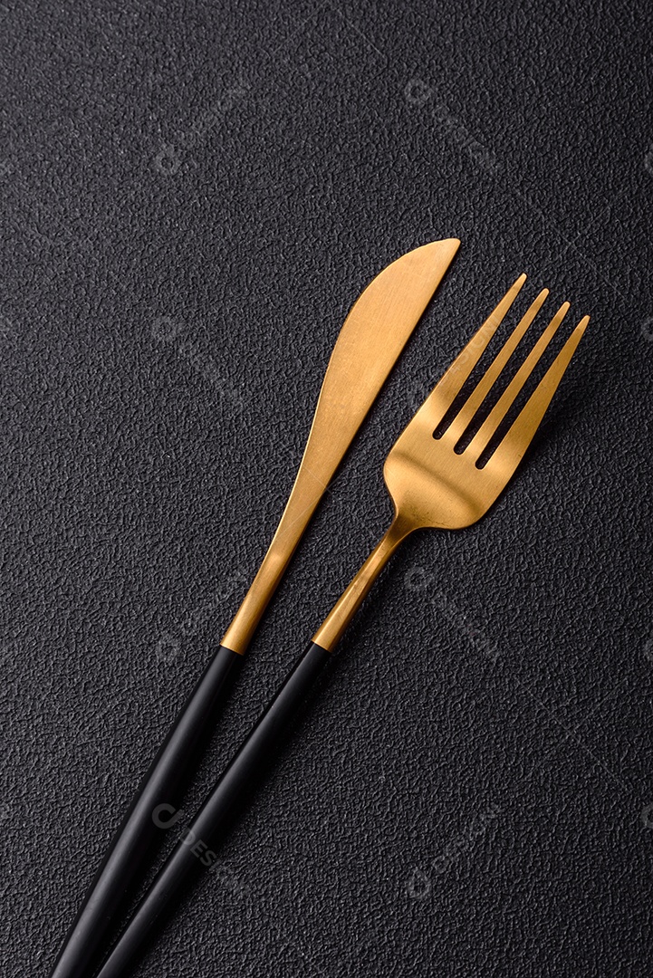 Garfo de talheres, faca e colher sobre um fundo de concreto texturizado escuro. Itens e acessórios de cozinha