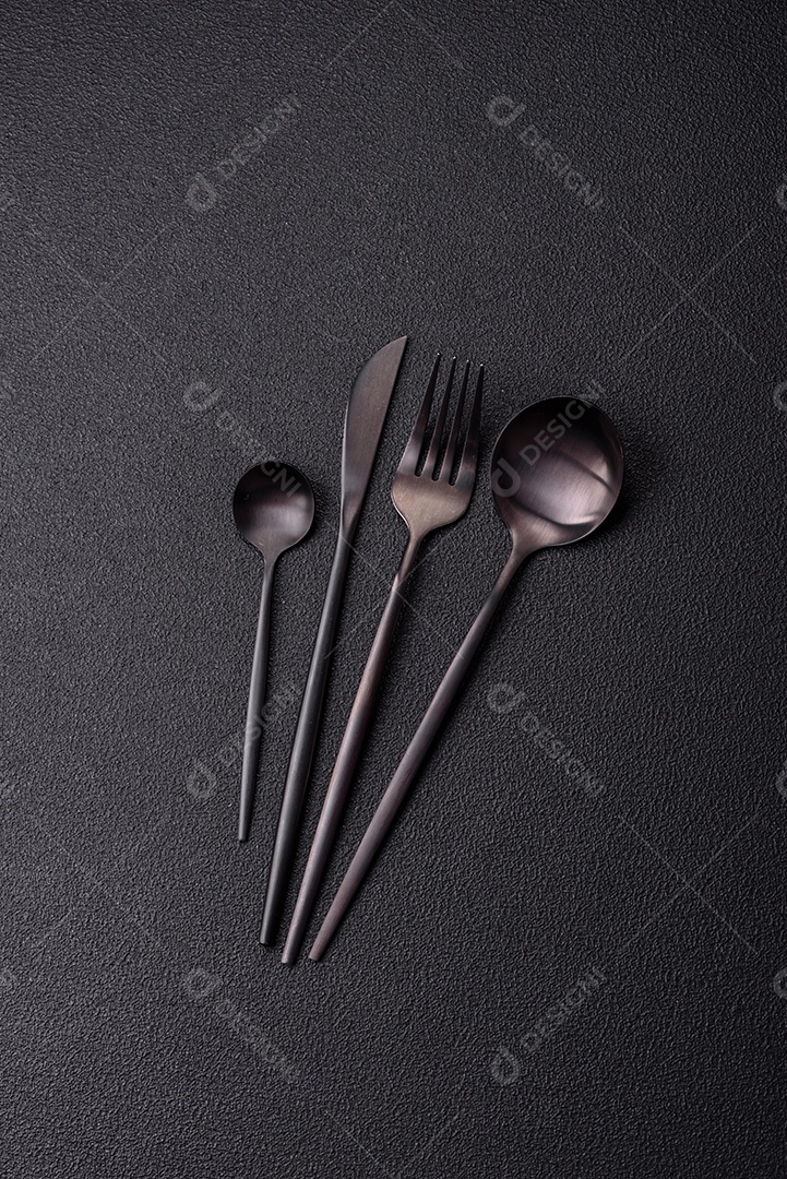 Garfo de talheres, faca e colher sobre um fundo de concreto texturizado escuro. Itens e acessórios de cozinha
