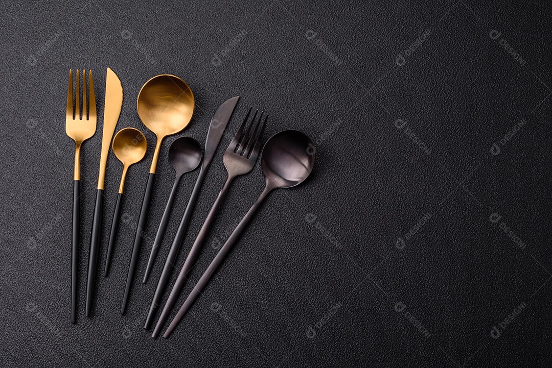 Garfo de talheres, faca e colher sobre um fundo de concreto texturizado escuro. Itens e acessórios de cozinha